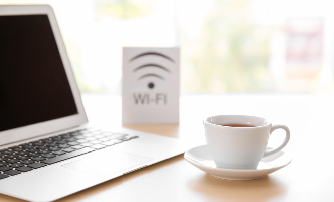 Laptop and WiFi sign next to a cup of coffee in a hotel room